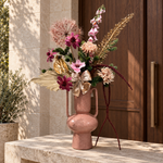 Blush Celebration: roze en paars zijden boeket met goudkleurige accenten, beige strik en bordeaux hangende takken in roze vaas met oren, entree
