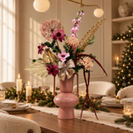 Blush Celebration: roze en paars zijden boeket met goudkleurige accenten, beige strik en bordeaux hangende takken in roze vaas met oren, kersttafel