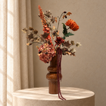 Zijden herfstboeket Caramel Harvest met oranje bloemen, roze hortensia, bruin blad en bordeaux hangende takken in karamelkleurige vaas op beige studioachtergrond