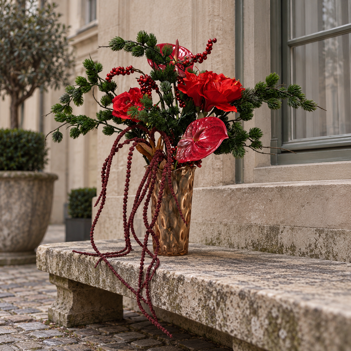Rood-groen zijden boeket Crimson Cascade in bronskleurige vaas op een stenen bank