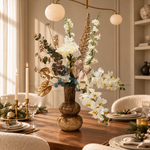 Wit-gouden zijden boeket met beige strik in bruine vaas op een gedekte kersttafel