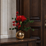 Ruby Glow met rode amaryllis, bessen en wintergroen in gouden bolvaas op een natuurstenen badkamermeubel