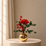 Klein zijden kerstboeket Ruby Glow met rode amaryllis, rode bessen en wintergroen in gouden bolvaas op beige studioachtergrond